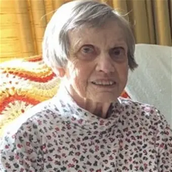 Smiling elderly woman in patterned shirt indoors.