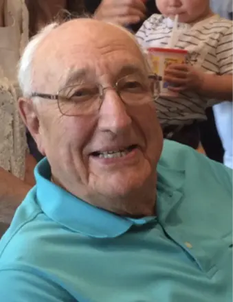 Smiling elderly man in glasses and blue shirt.