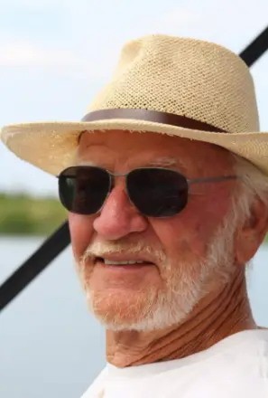 Elderly man wearing sunglasses and straw hat outdoors.