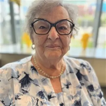 Elderly woman in floral dress, wearing glasses.