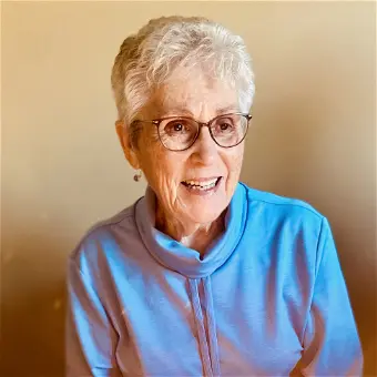 Smiling person with glasses and blue sweater.