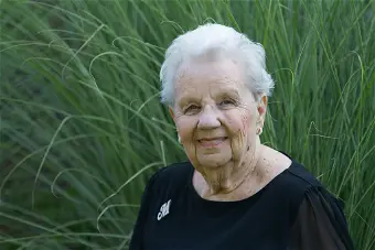 Elderly woman smiling in front of tall grass.