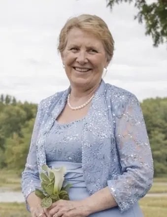 Smiling woman in blue lace dress holds white flower.