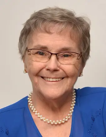 Smiling elderly woman with glasses and blue dress.