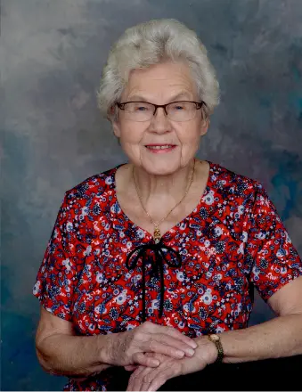 Elderly woman smiling in red floral blouse.