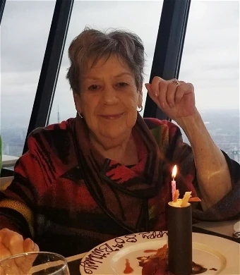 Woman celebrating birthday with candlelit dessert.