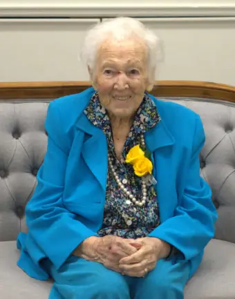 Elderly woman in blue suit with yellow flower