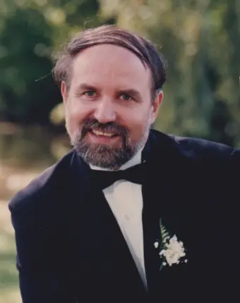 Smiling man in tuxedo with boutonniere outdoors.