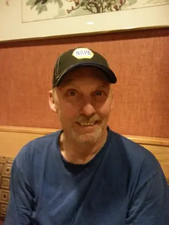 Smiling man wearing a NAPA cap indoors.