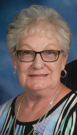 Elderly woman smiling with glasses and striped blouse.