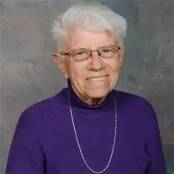 Smiling elderly person wearing glasses and purple sweater.