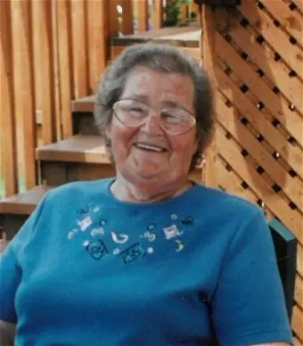 Smiling elderly woman sitting outdoors on wooden deck.