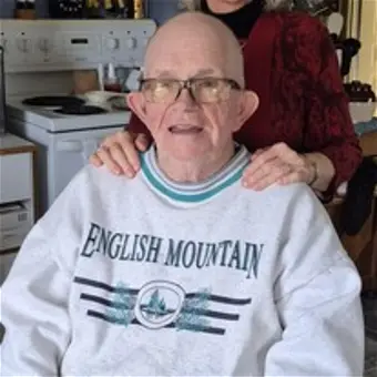 Elderly man smiling with person's hands on shoulders.