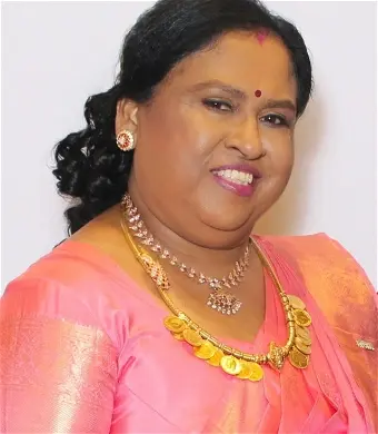 Smiling woman in pink saree and gold jewelry.