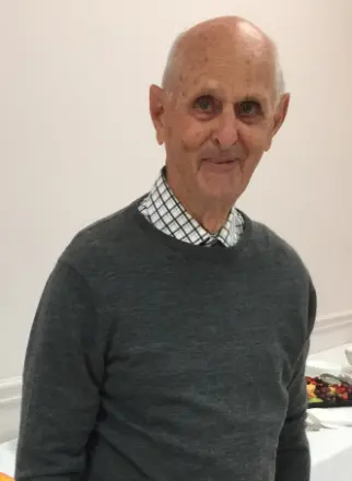 Elderly man smiling wearing gray sweater indoors