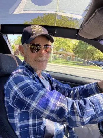 Smiling man driving car wearing sunglasses and cap.