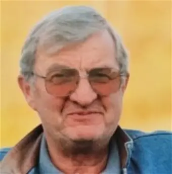 Smiling elderly man with glasses and denim jacket.