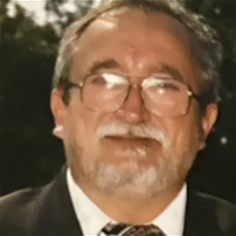 Man in suit and glasses smiling outdoors.