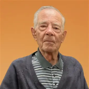 Elderly man in striped shirt against orange background.
