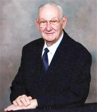 Elderly man in suit with glasses, smiling portrait.