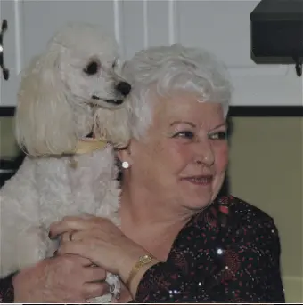 Smiling woman holds small white dog indoors.