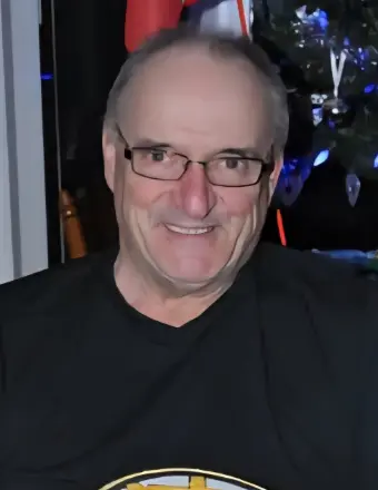 Smiling man wearing glasses and black shirt indoors.