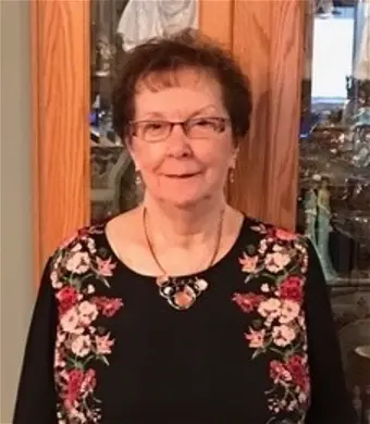 Smiling woman in floral shirt stands indoors.