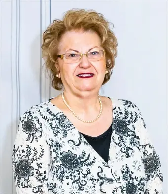 Elderly woman smiling with floral blouse and glasses.