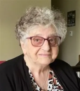 Elderly woman with glasses, smiling indoors.