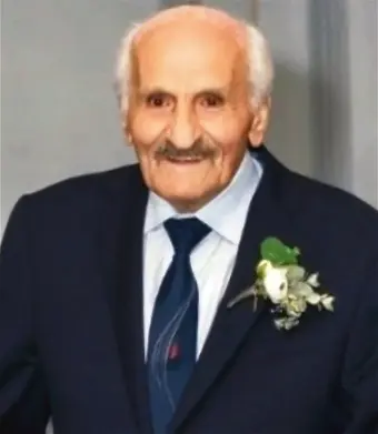 Elderly man in suit with boutonniere smiling.