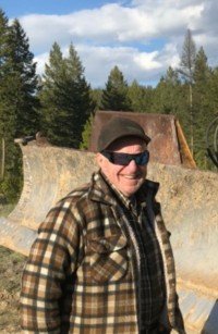 Man outdoors by machinery, wearing plaid and sunglasses.