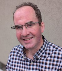 Man wearing glasses and a checked shirt smiling.