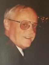 Elderly man with glasses smiling in dim lighting.