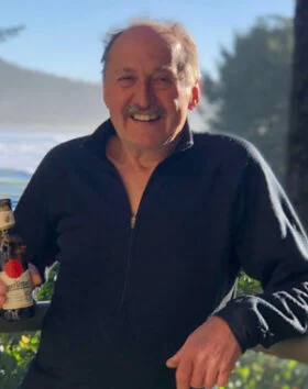 Smiling man holding a bottle outdoors.