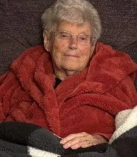 Elderly woman in red blanket resting indoors.