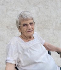 Elderly woman sitting against a textured wall.