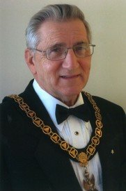 Elderly man in formal wear with gold chain.