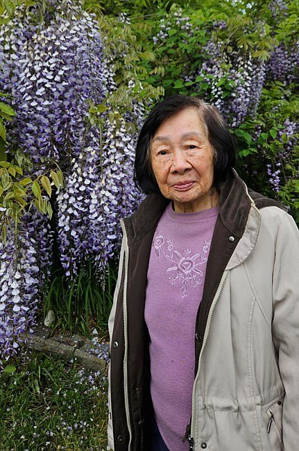 Woman standing by purple wisteria flowers.