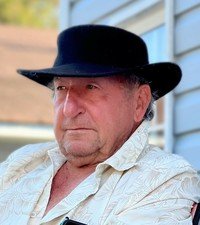 Man in hat and patterned shirt outdoors.
