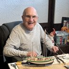 Man happily building a model ship at desk.