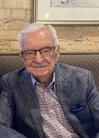 Older man in glasses and blazer smiling indoors.