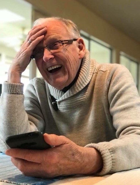 Elderly man laughing while holding smartphone indoors.