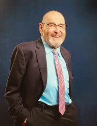 Smiling man in suit with blue shirt, pink tie.