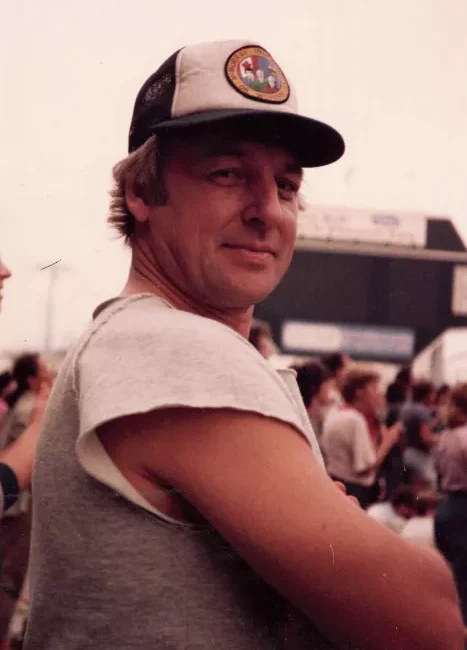 Man in cap at outdoor event, smiling.
