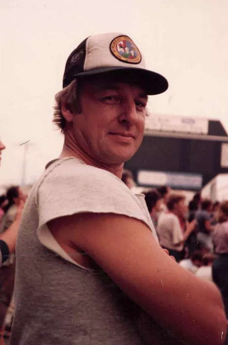 Man in cap at outdoor event, smiling.