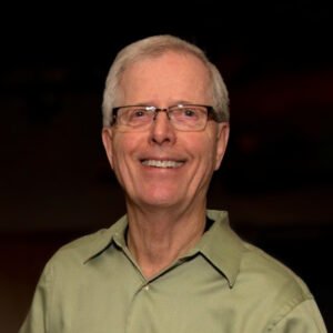 Smiling elderly man in glasses and green shirt.