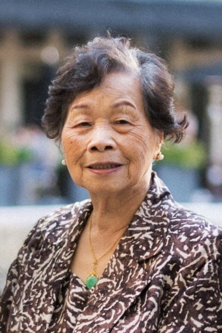 Elderly woman smiling outdoors in patterned jacket.