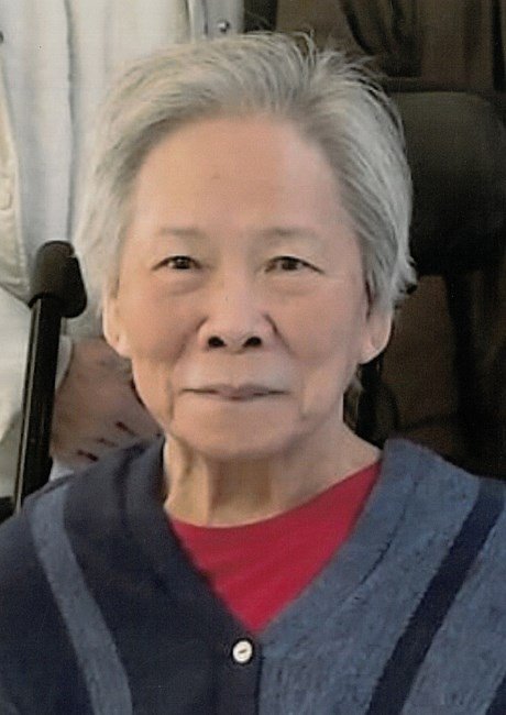 Elderly person smiling, wearing blue and red sweater.