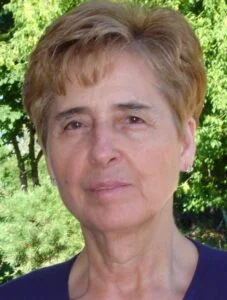 Person outdoors with short hair and trees background.