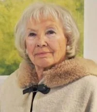 Elderly woman in fur coat, smiling slightly.